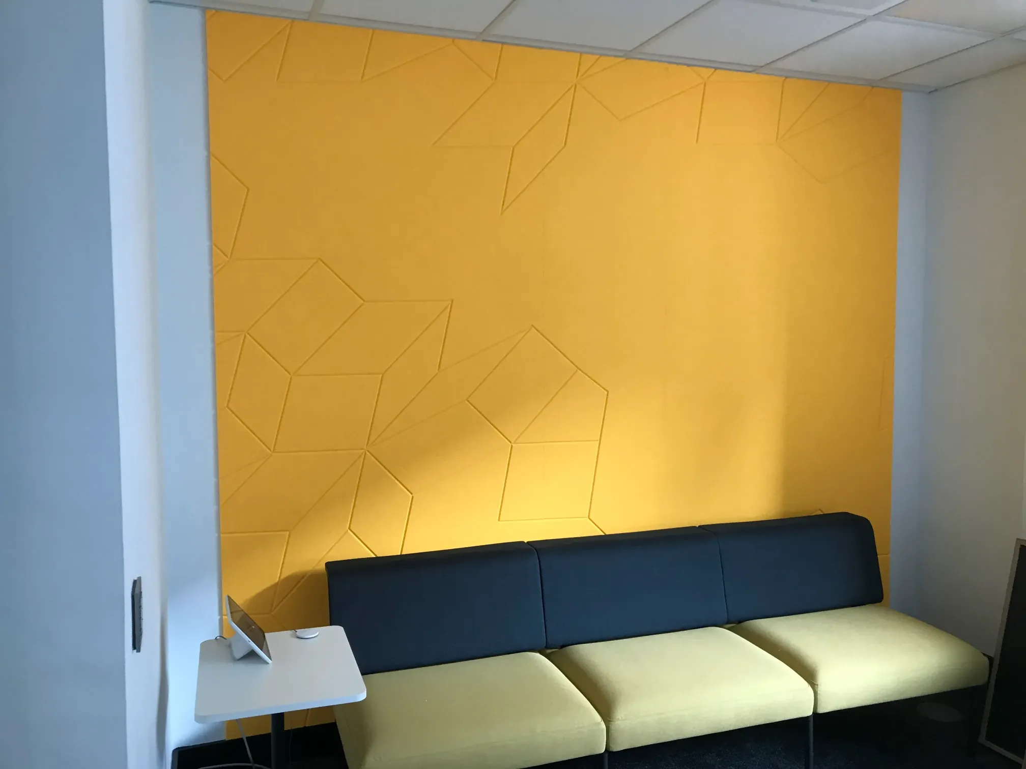 Yellow acoustic wall panelling with a blue cream couch.